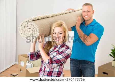 Happy Young Couple Carrying Rolled Carpet In Their New Home