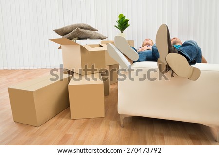 Couple Sleeping On Couch In New Home With Cardboard Boxes Around