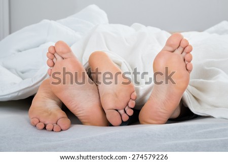 Feet Of Couple With Blanket In Bed