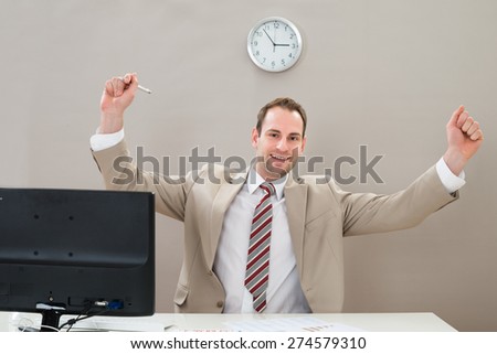 Happy Businessman Raising Hand At Desk In Office