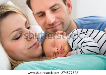 Close-up Of Two Parents Looking At Newborn Sleeping Baby