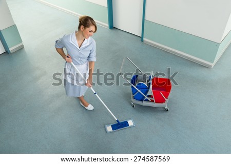 Happy Female Janitor With Mop And Cleaning Equipment On Floor
