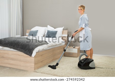 Female Housekeeper Cleaning Rug With Vacuum Cleaner In Hotel Room