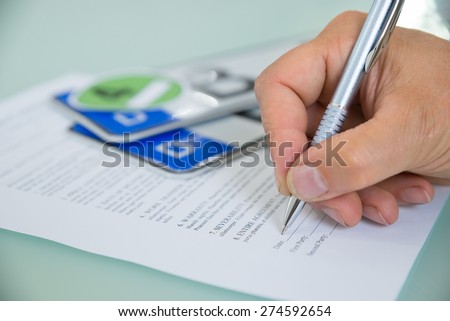 Close-up Of A Hand Filling Car Sale Contract Form With Vehicle Registration Plate On Desk. Contract Paper Contains Placeholder Text