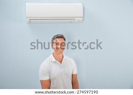 Portrait Of A Happy Mid-adult Man Standing Under Air Conditioner