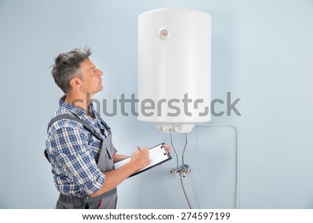 Portrait Of Mid-adult Male Plumber Holding Clipboard Looking At Electric Boiler
