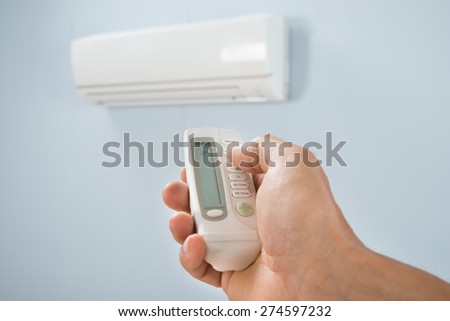 Man Adjusting Temperature Of Air Conditioner Using Remote