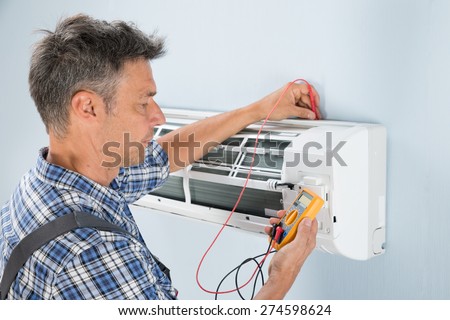 Portrait Of A Mid-adult Male Technician Testing Air Conditioner With Digital Multimeter