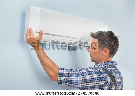 Portrait Of A Mid-adult Male Technician Fixing Air Conditioner On Wall