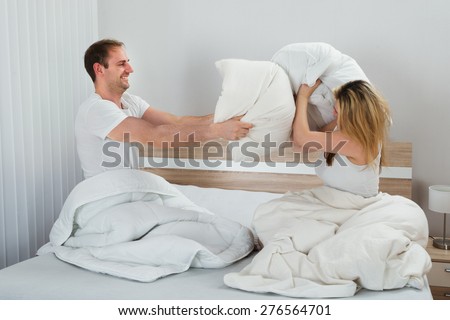 Happy Couple Fighting Together With Pillows On Bed