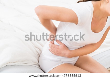 Close-up Of Female Sitting On Bed Having Backache