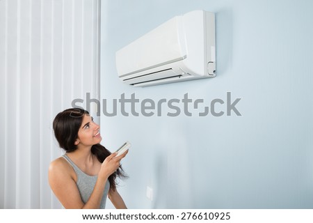 Young Happy Woman Holding Remote Control Air Conditioner In House