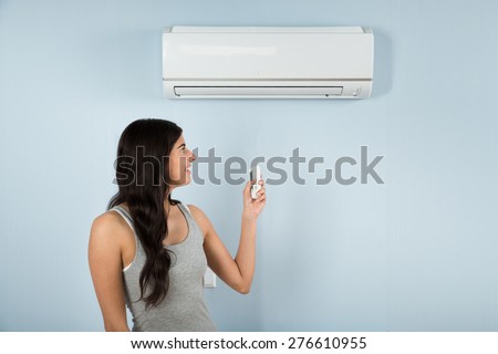 Young Happy Woman Using Remote Control Of Air Conditioner