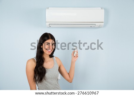 Happy Woman Holding Remote Control In Front Of Air Conditioner At Home