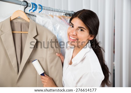 Female Cleaner In Laundry Shop Removing Lint From Clothes With Adhesive Roller