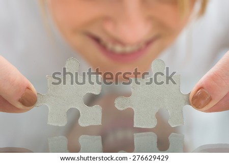 Portrait Of Happy Businesswoman Holding Pieces Of Jigsaw Puzzle On Desk