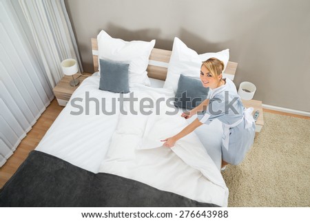 Female Housekeeper Making Bed With Bed Clothes In Hotel Room