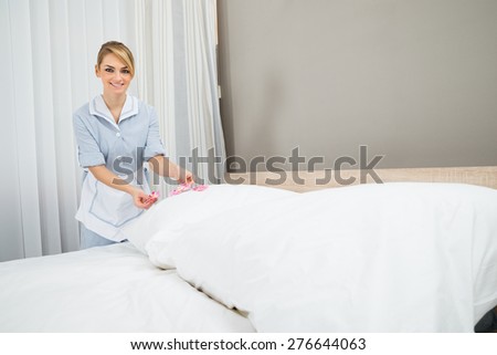 Happy Female Housekeeper Decorating Bed With Petals