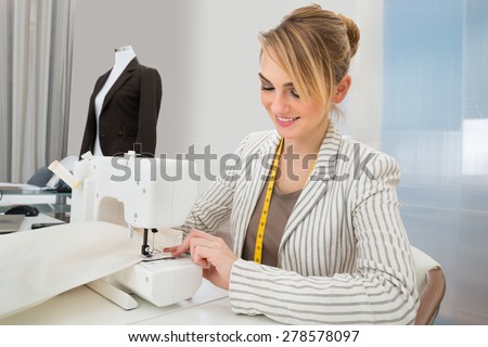 Portrait Of Beautiful Fashion Designer Working On Sewing Machine In Studio