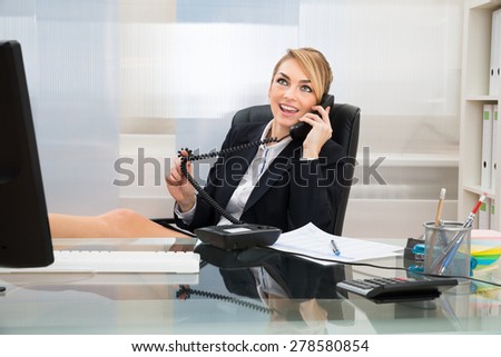 Young Happy Businesswoman Talking On Landline Phone At Desk