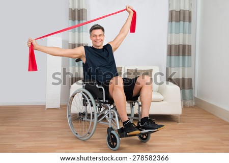 Handicapped Man On Wheelchair Exercising With Resistance Band At Home