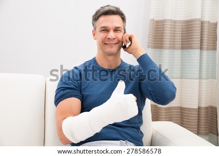 Man With Fractured Hand Sitting On Sofa Talking On Cellphone