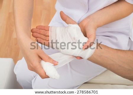 High Angle View Of A Female Doctor Bandaging Patient\'s Hand