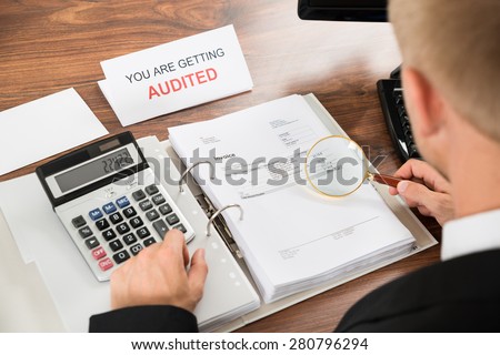 Close-up Of A Male Auditor Checking Invoice Using Magnifying Glass And Calculator