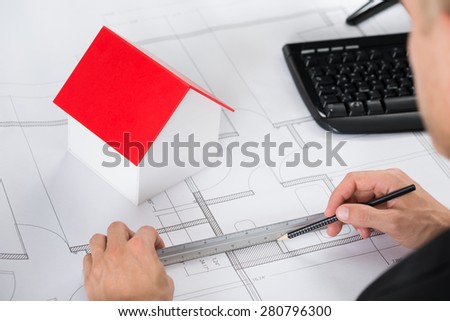 Close-up Of Architect With House Model Making Blueprint