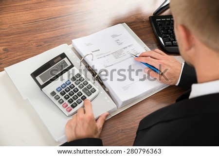 Close-up Of A Businessman Calculating Invoice Using Calculator At Desk In Office