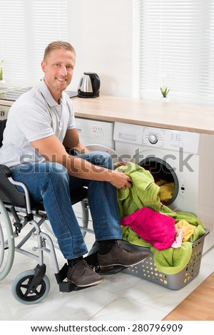 Young Happy Man On Wheelchair Putting Clothes Into The Washing Machine