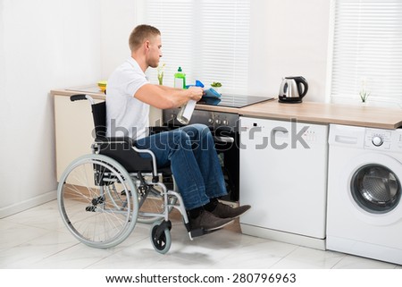 Young Handicapped Man On Wheelchair Cleaning Induction Stove