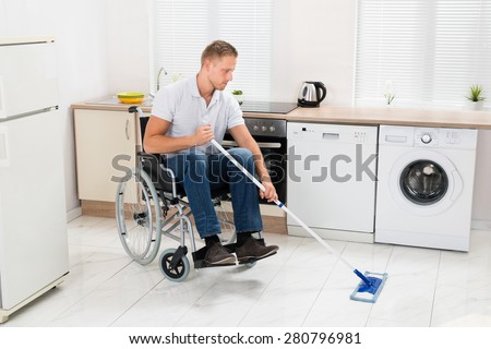 Disabled Man On Wheelchair Cleaning Floor With Mop In Kitchen Room