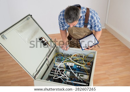 Electrician Looking At Fuse Box Holding Clipboard