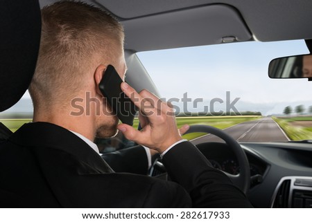 Rear View Of A Businessman Talking On Cellphone While Driving Car