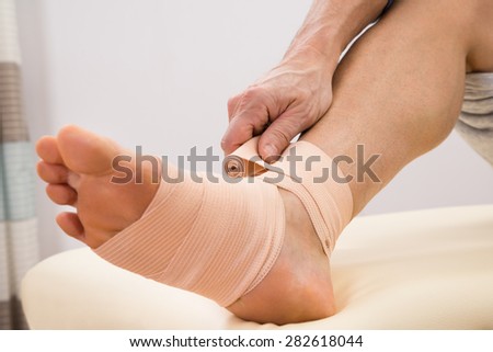 Close-up Of A Man Putting Elastic Bandage On His Injured Foot