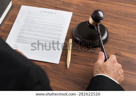 Close-up Of Judge Hitting The Gavel With Contract Paper At Desk