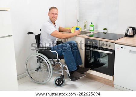 Young Happy Disabled Man On Wheelchair Washing Dishes