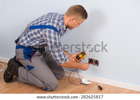 Male Electrician Checking Voltage Of Socket With Multimeter In House