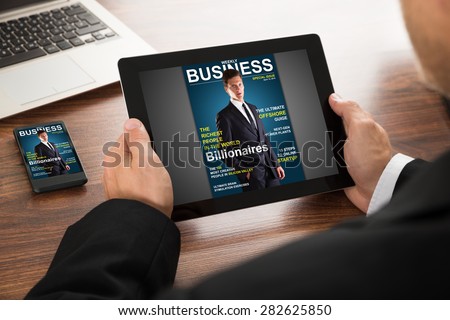 Close-up Of A Businessman Reading Online Magazine On Digital Tablet And Cellphone