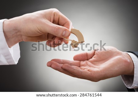 Close-up Of A Doctor\'s Hand Giving Hearing Aid To Patient