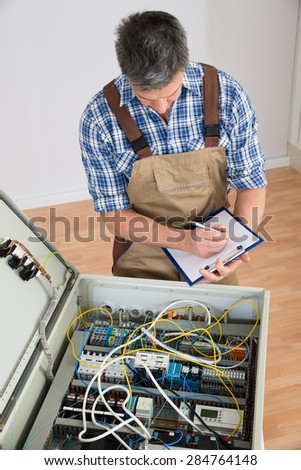 Electrician Looking At Fuse Box Holding Clipboard