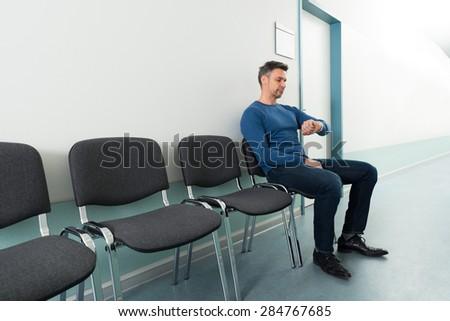 Mid-adult Man Looking At Wrist Watch Sitting In Hospital