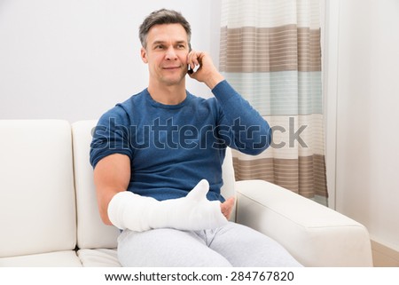 Man With Fractured Hand Sitting On Sofa Talking On Cellphone