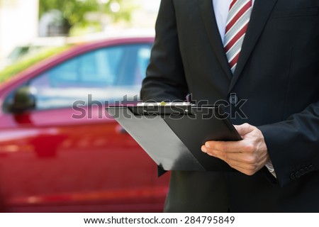 Close-up Of A Man Standing In Front Of Car Holding Clipboard In His Hand