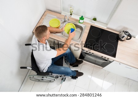 High Angle View Of Disabled Man On Wheelchair With Sponge Washing Dishes