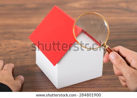 Close-up Of Person Hands With Magnifying Glass Inspecting A Model House
