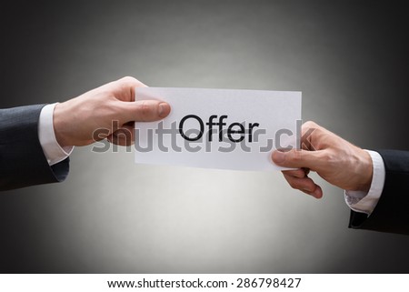 Close-up Of Two Businessman\'s Hand Holding Paper With Text Offer