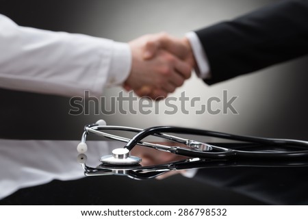 Doctor And Businessman Shaking Hand In Front Of Stethoscope