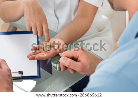 Close-up Of Young Female Doctor Showing Hearing Aid To Male Patient In Clinic